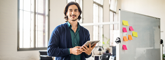 man wearing a blue cardigan holding a tablet in his studio office