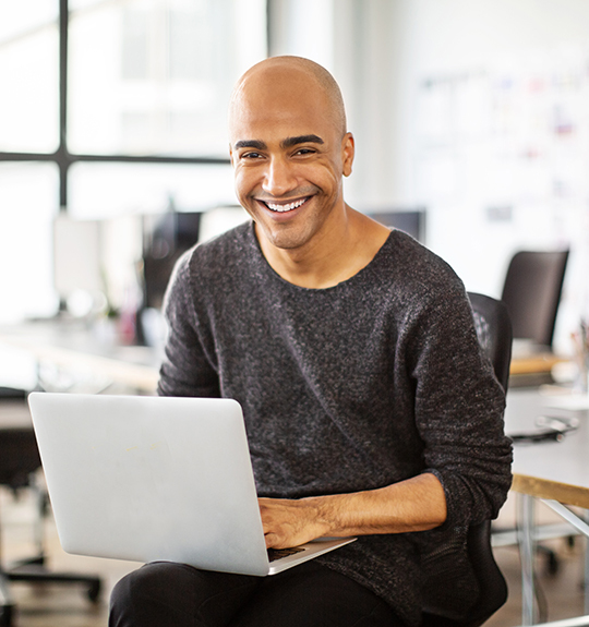 man smiling working on a laptop in an office