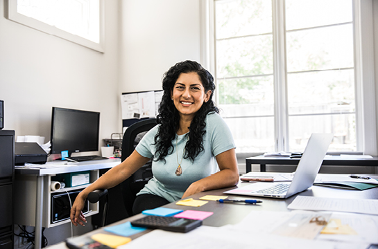 Woman smiling in her office, various colorful sticky notes stuck to her desk