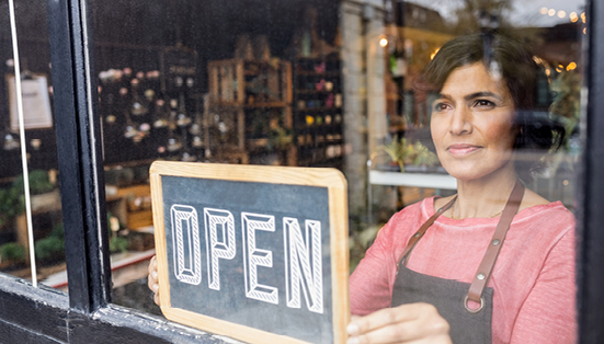 woman behind a windowfront, flipping a sign to Open