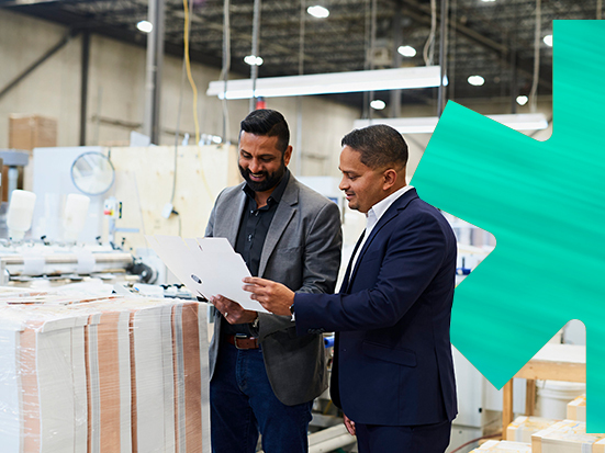 Two men examining a document in a factory with a blue leaf in the background