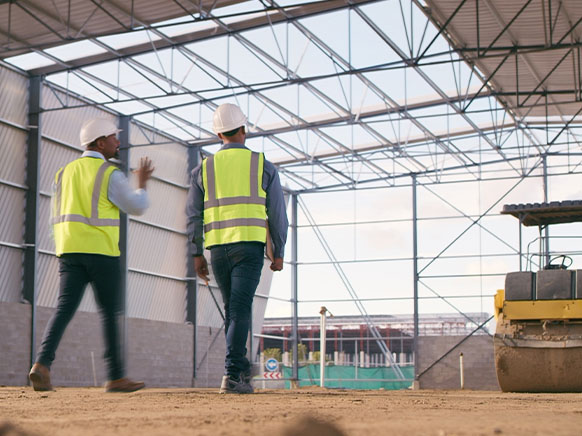 two men walking in yellow hi-vest in a building in construction