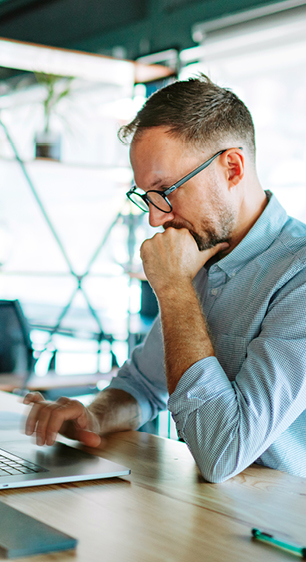 Man wearing glassing and typing on his laptop in modern office