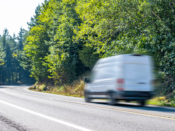 White cargo van on a road next to a forest