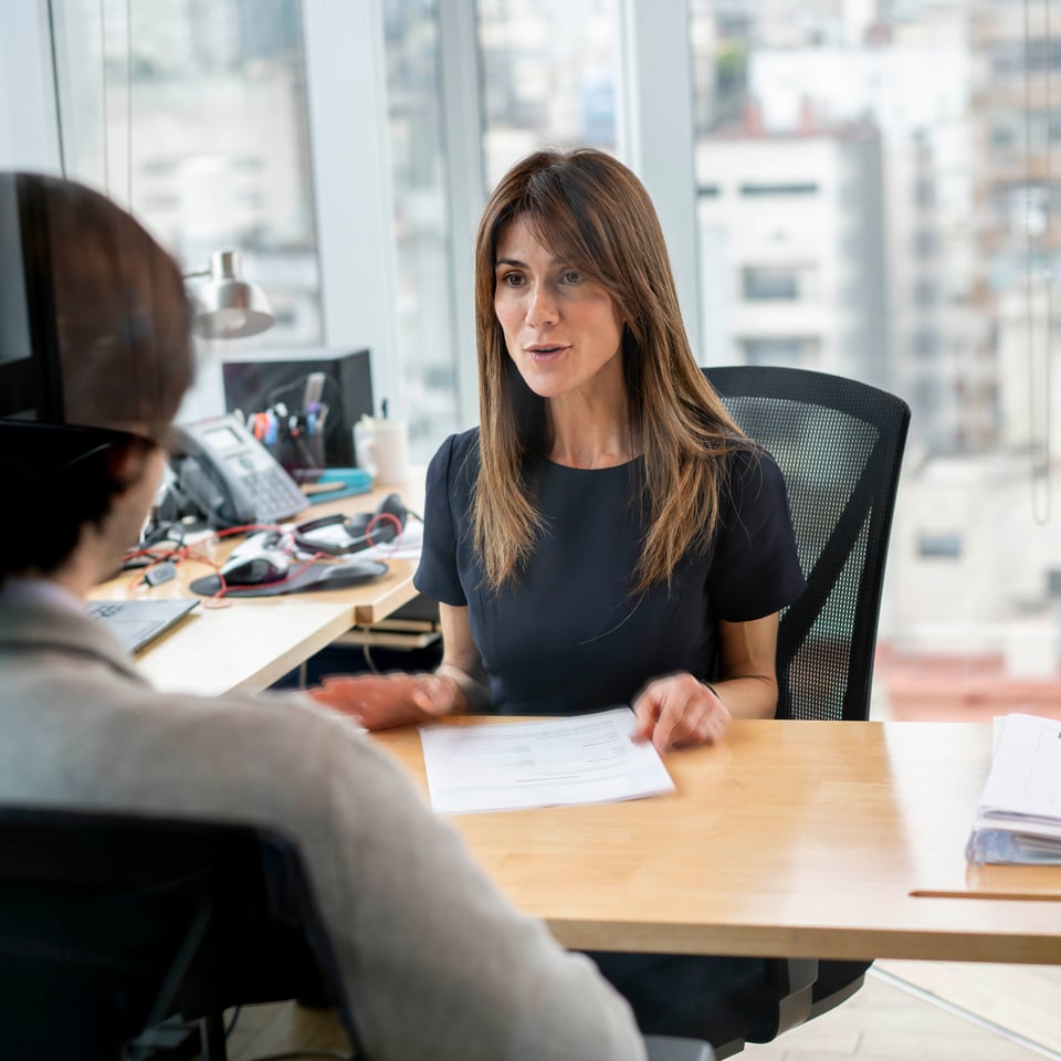 HR manager at her office talking to employee cheerfully while holding some paperwork